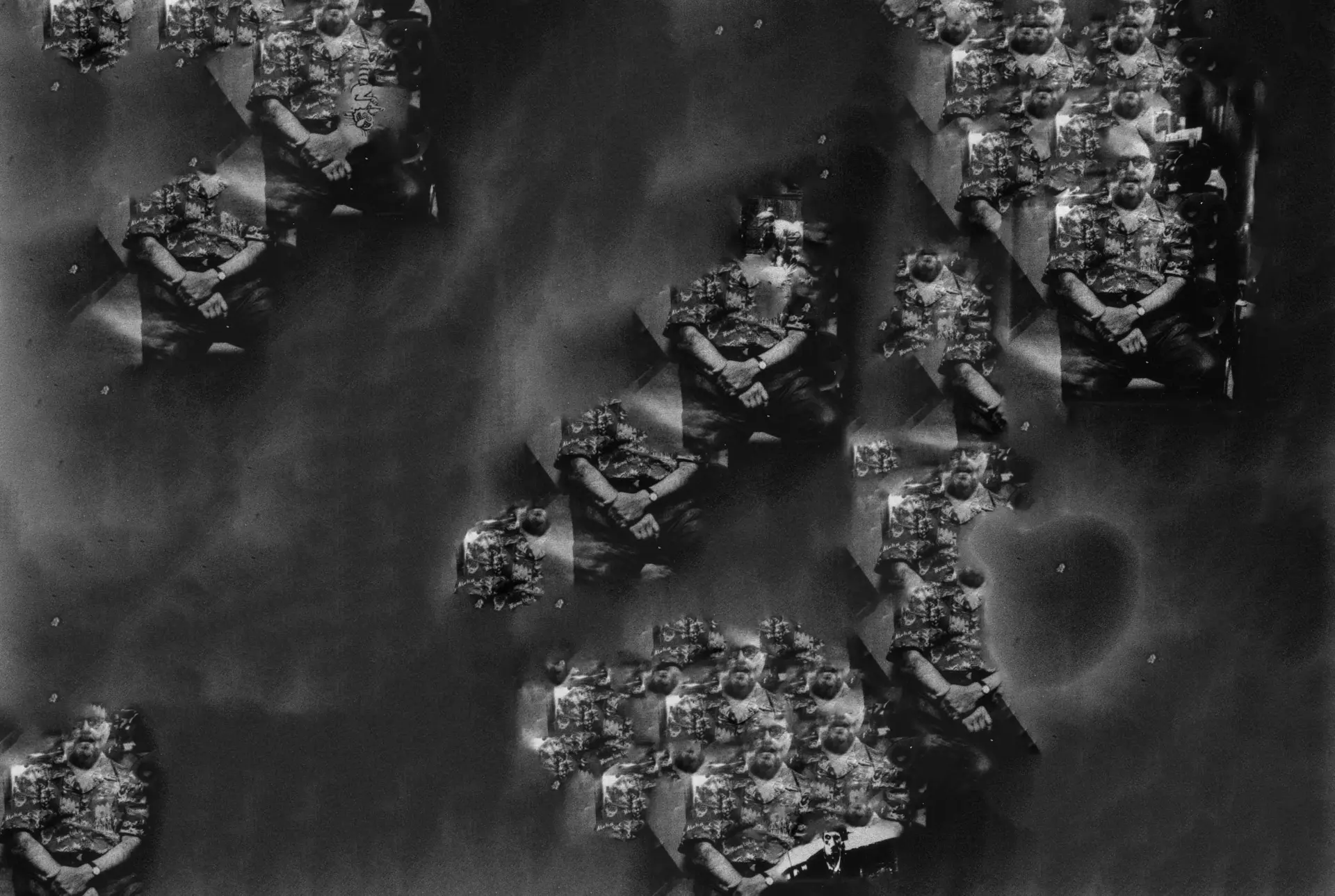 Cette photographie argentique en noir et blanc, datant de décembre 1999, capture l’intérieur d’une pièce. Une porte est recouverte de diverses affiches, photographies et notes. Deux chaises sont visibles au premier plan, suggérant un espace de vie. Le mur à gauche de la porte présente d’autres notes et ce qui semble être un calendrier. Un manteau est accroché sur le côté supérieur gauche, et une ombre distincte se dessine sur la porte, ressemblant à un profil humain. L’ambiance de la pièce évoque des souvenirs personnels ou une histoire vécue.